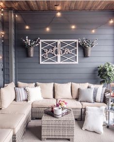 an outdoor living room with couches, tables and lights on the side of the house