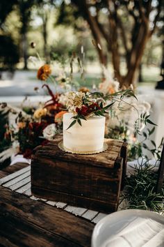 a white cake sitting on top of a wooden box next to flowers and greenery