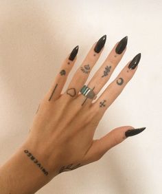 a woman's hand with black nail polish and tattoos on her left wrist, holding up an open ring