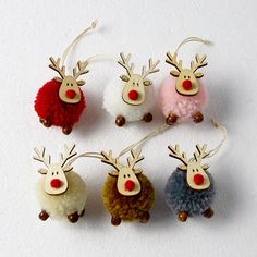 six different colored reindeer ornaments hanging from strings on a white surface with brown and red pom - poms