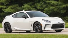 a white sports car driving down a road next to green grass and trees in the background