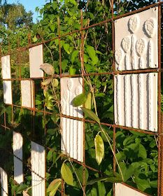 several white tiles are attached to a wire fence with vines growing on it and some green leaves in the foreground