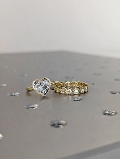 two wedding rings sitting on top of a metal surface with dots around them and one has a heart shaped diamond in the middle