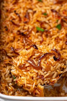 a spoon full of rice with onions and mushrooms on it in a casserole dish