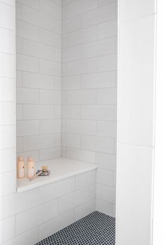 a white tiled bathroom with black and white floor tiles on the shower wall, along with candles