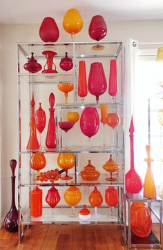 an assortment of colorful vases on display in a room with wooden floors and white walls