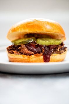 a pulled pork sandwich with pickles and ketchup on a white platter