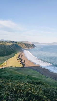 the beach is next to an ocean and grassy hill