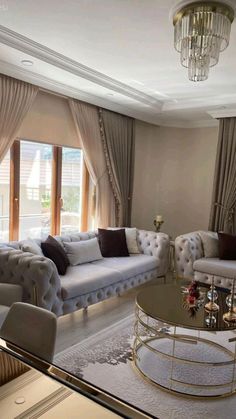 a living room filled with furniture and a chandelier above a glass coffee table