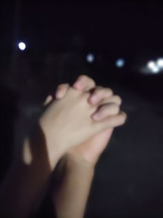 a person holding their hand up in the air at night with bright lights behind them