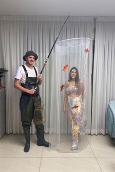 a man and woman dressed up as fish with fishing rods in their hands, standing next to each other