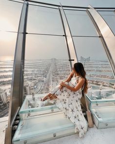 a woman sitting on top of a tall glass building looking out at the city below