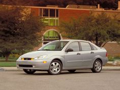 a silver car is parked in front of a building with trees and bushes behind it