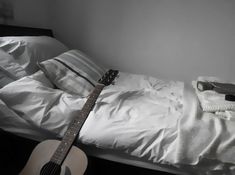 a guitar laying on top of a bed next to pillows and blankets in a room