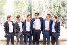 a group of men standing next to each other in front of a water fountain wearing suits and ties