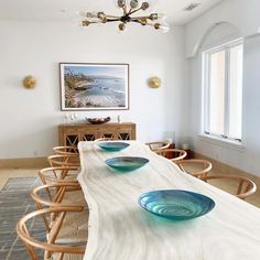 a long table with blue glass bowls on it in front of a painting and chandelier