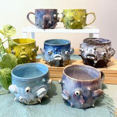 five ceramic mugs with eyes and mouths are on the table next to each other