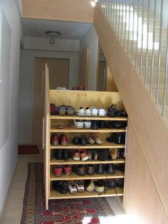 there are many pairs of shoes on the shelf under the stairs in this hallway area