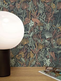 a lamp sitting on top of a wooden table next to a book and glasses in front of a wallpaper