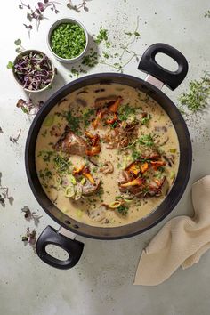 a pot filled with soup next to bowls of vegetables and herbs on a white surface