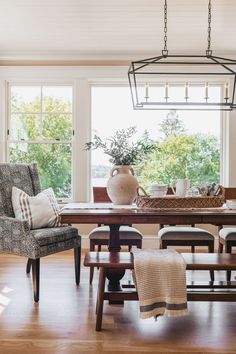 a dining room table with chairs and a bench in front of it, next to a large window