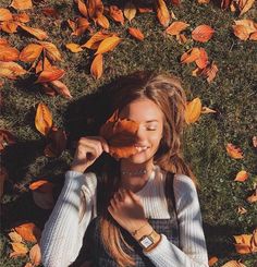 a woman laying in the grass with leaves on her face and holding a piece of food up to her mouth