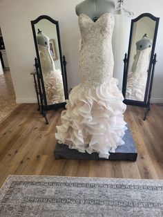 a wedding dress is displayed on a mannequin in front of two mirrors and a rug