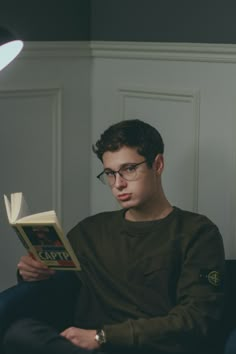 a young man reading a book while sitting on a couch in front of a lamp