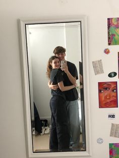 a man and woman standing in front of a mirror taking a selfie with their cell phone