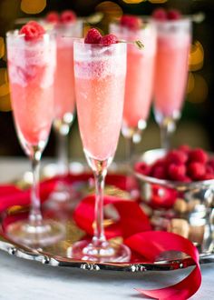 three champagne flutes with raspberries in them on a silver tray and red ribbon