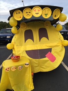 a large yellow car with many smiley faces on it's hood and some tables in the parking lot