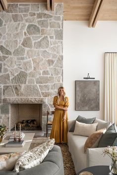 a woman standing in the middle of a living room next to a stone wall and fireplace