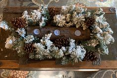 pine cones and candles are arranged in a wreath on top of a wooden board with snow flakes