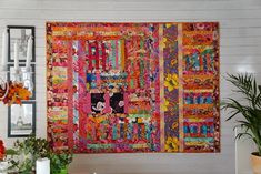 a colorful quilt hanging on the wall next to a potted plant and vases