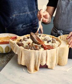 two people in aprons are preparing food on a table with bowls and spoons