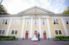 a bride and groom standing in front of a yellow building with white columns on it