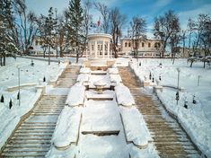 a snow covered park with benches in the foreground and a building in the background