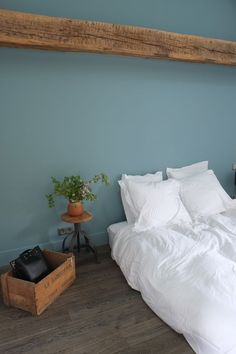 a bed with white linens and pillows in a blue room next to a plant