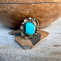 This vintage ring stands out for the beautiful bright blue natural turquoise stone set in a somewhat ornate border/foundation is typical of Navajo jewelry from the 1960s. The ring is on the medium to medium-large size, and with that stone that is the color we've come to associate with the word "turquoise," the ring does get noticed. Great piece for the person who loves authentic jewelry and authentic vintage. No hallmark, but that is not unusual as Native American hallmarks really began to appear in the 1970s. Some tarnish on the back, which I am happy to polish. Just let me know.      The ring face measures about 1" wide by 1-1/8" tall. Is a Size 8. Weighs 11g. The stone rocks ever so slightly yet is well seated.  A great piece for the old soul. Note that due to lighting plus monitor sett Bohemian Turquoise Ring With Patina For Collectors, Untreated Blue Turquoise Western Ring, Southwestern Style Untreated Blue Turquoise Ring, Bohemian Blue Rings With Concho, Bohemian Blue Rings With Concho Detail, Southwestern Blue Turquoise Ring With Patina, Southwestern Turquoise Ring With Concho, Bohemian Blue Concho Rings, Blue Bohemian Concho Ring