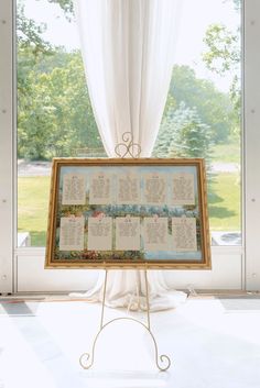 a wedding seating chart on a stand in front of a window with white drapes