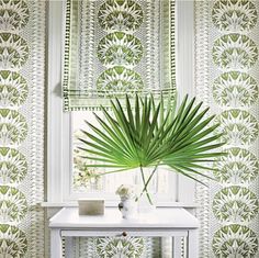 a white table sitting next to a window covered in green wallpaper and a palm leaf