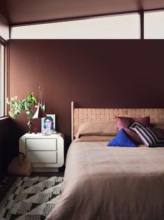 a bed sitting next to a window in a room with brown walls and pillows on top of it