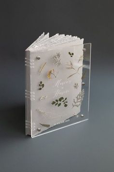 a clear book with pressed flowers and leaves on the cover is shown in front of a gray background