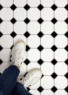 a person wearing white tennis shoes standing on a black and white tiled floor