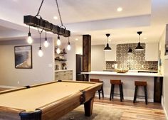 a pool table in the middle of a living room with bar stools around it