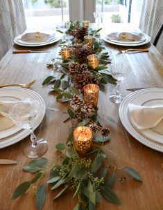 a long table with pine cones, greenery and candles is set for a festive dinner