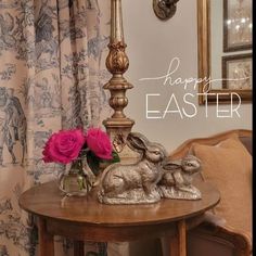 a wooden table topped with two silver rabbits next to a vase filled with pink roses