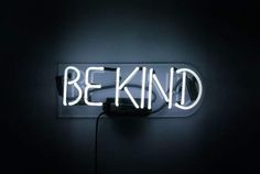 a neon sign that says be kind in the middle of a dark room with a cord plugged into it