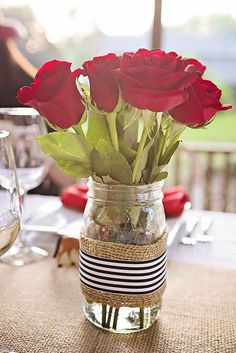 red roses in a mason jar on a table with place settings and wine glassware