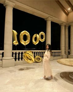 a woman standing in front of columns with balloons that spell out the number 100 on them